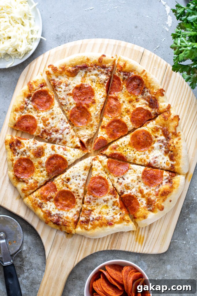 A cooked and cut pizza showing of how to make home pizza on a wooden pizza peel surrounded by ingredients.
