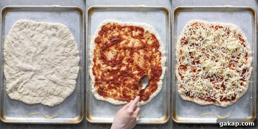 A pizza on a sheet pan being topped with sauce and cheese.