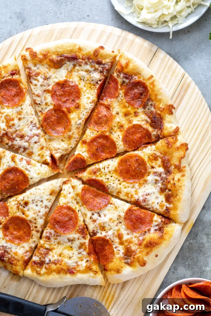 Close up of a freshly cooked and cut pizza on a wooden pizza peel showing melted cheese and cooked pepperoni.