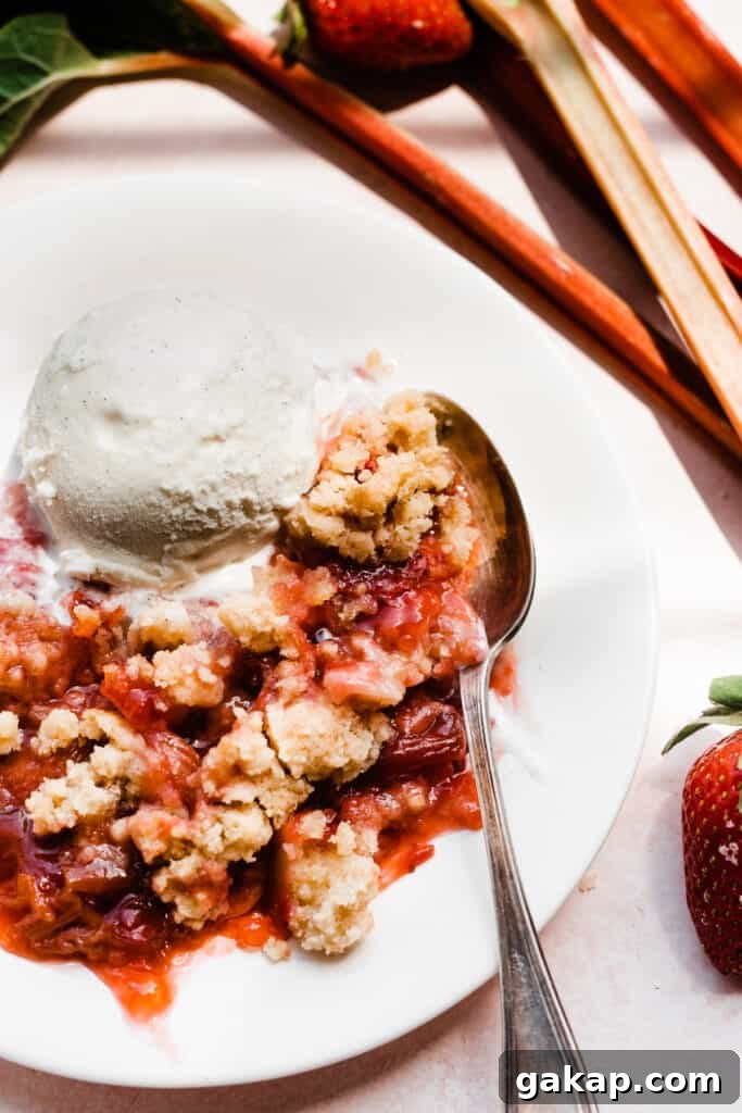A spoon digging into a serving of strawberry rhubarb crumble on a plate.