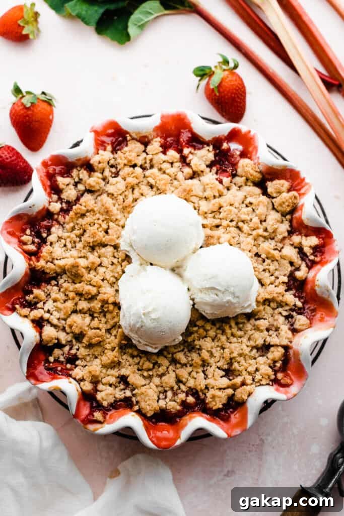 Baked strawberry rhubarb crumble topped with scoops of ice cream.