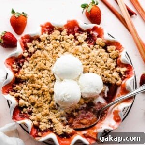 Strawberry rhubarb crumble in a pie dish topped with scoops of ice cream.