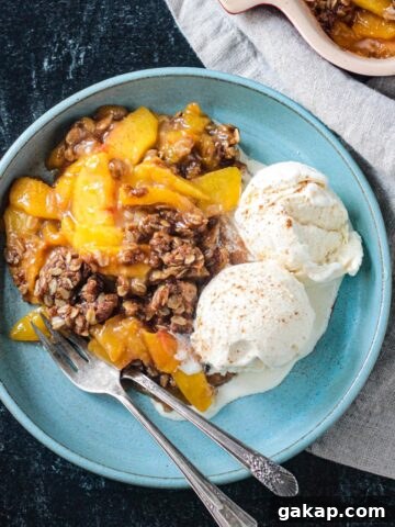 Vegan peach crisp with two scoops of vanilla ice cream on a blue plate.