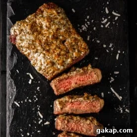 A parmesan crusted steak partially sliced on a black, stone platter.