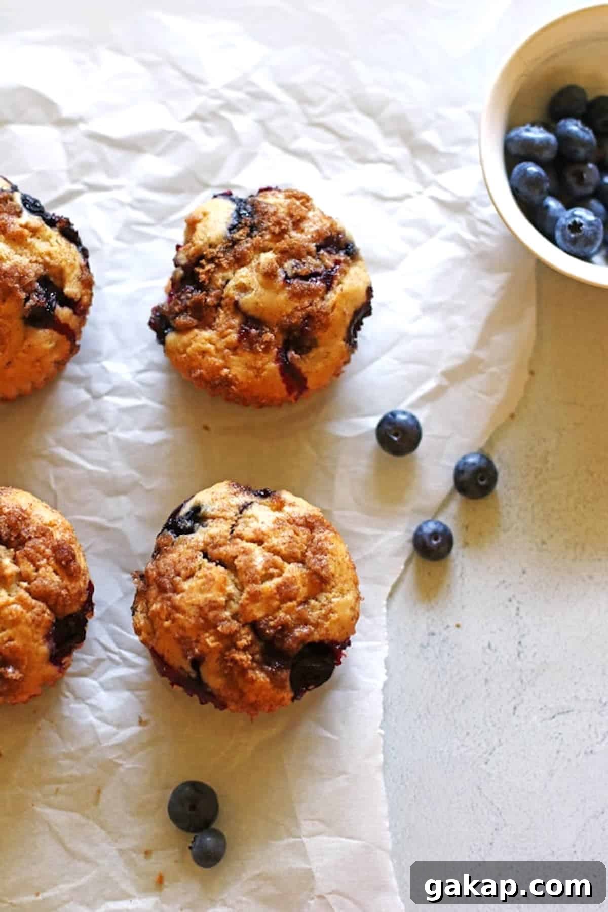 Blueberry Muffins on white parchment paper with a small bowl of blueberries next to them