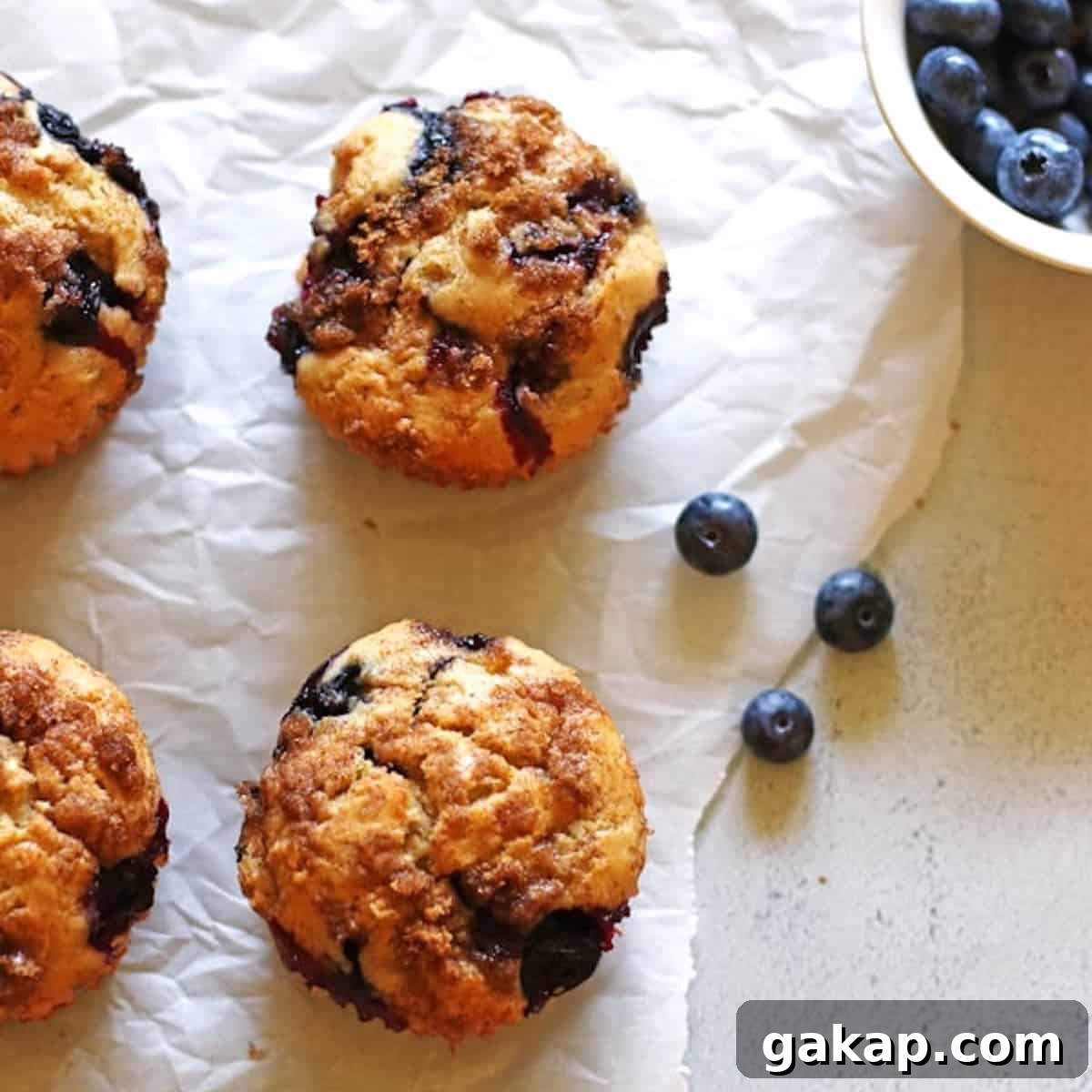 Blueberry Banana Muffins on white parchment paper with a small bowl of blueberries next to them.