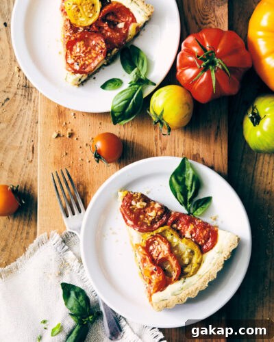 Two pieces of heirloom tomato tart on a serving board with heirloom tomatoes