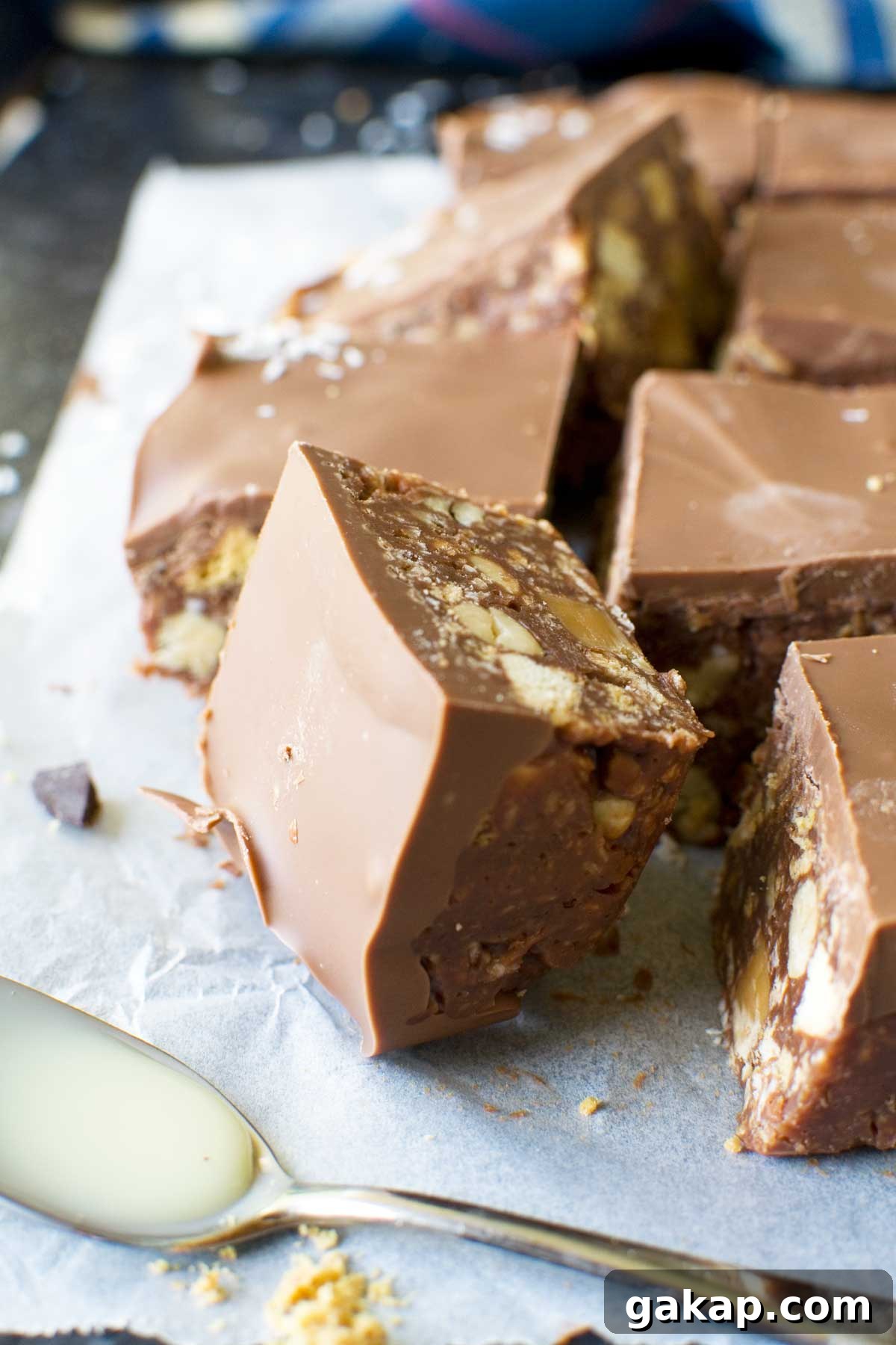 A square of hedgehog slice on its side on baking paper and with more in the background and a spoon with condensed milk in the foreground