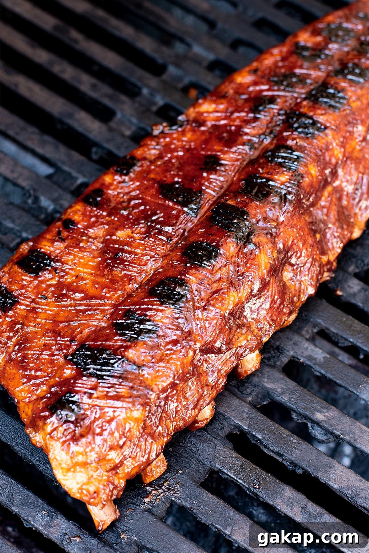 Juicy Oven-Baked BBQ Ribs Recipe for Tender, Fall-Off-the-Bone Meat 6 Charred baby back ribs being finished on a grill with BBQ sauce
