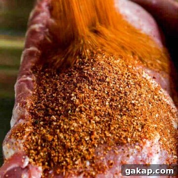 A large pork loin roast with a lot of dry rub seasoning pouring over the top.