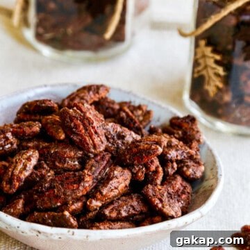 A white bowl with candied pecans and a few on the table with jars filled with them nearby.