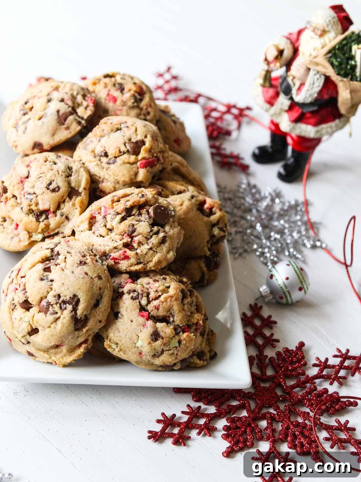 A white rectangle plate filled with chocolate chip peppermint cookies with a small Santa nearby.