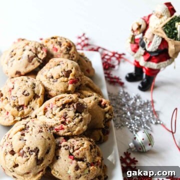 A white rectangle plate filled with chocolate chip peppermint cookies with a small Santa nearby.