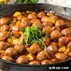 A skillet of sweet and sour meatballs in a brown sauce, garnished with green onions and mixed with vibrant red and yellow bell peppers.