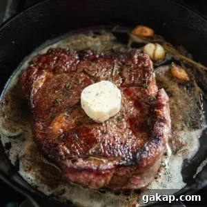 A ribeye cooking a cast iron skillet with a pat of herb and garlic butter on top.