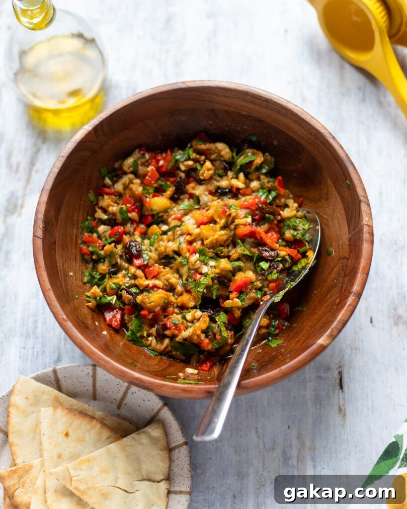 Overhead view of a bowl of eggplant salad, a side of pita bread and some extra virgin olive oil