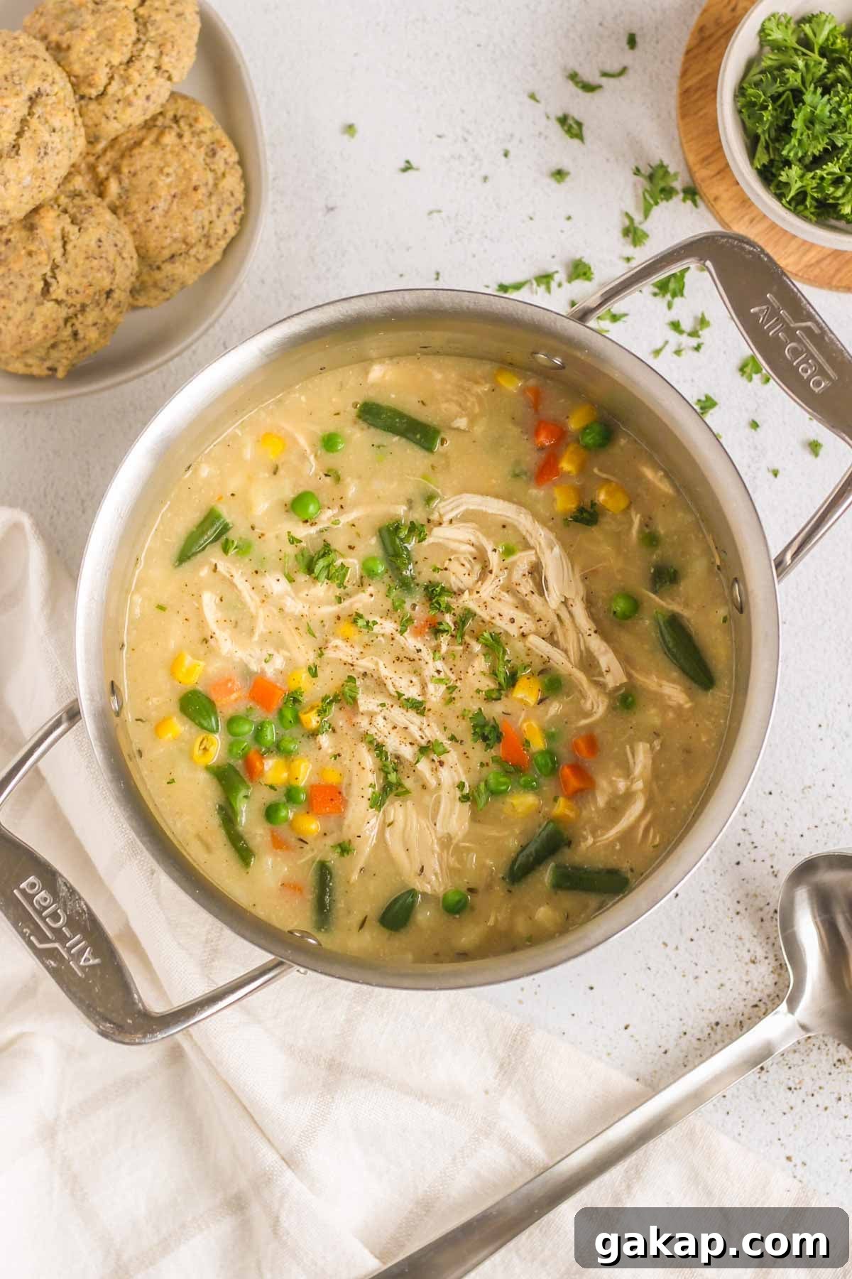 Dairy-Free, Gluten-Free Chicken Pot Pie Soup Recipe 2 Chicken pot pie soup in a stainless steel stock pot with a plate of biscuits and a soup ladle on the side.