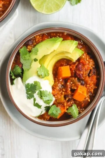 Vegetarian sweet potato topped with avocado, cilantro, and sour cream in a dark bowl sitting on a white plate.