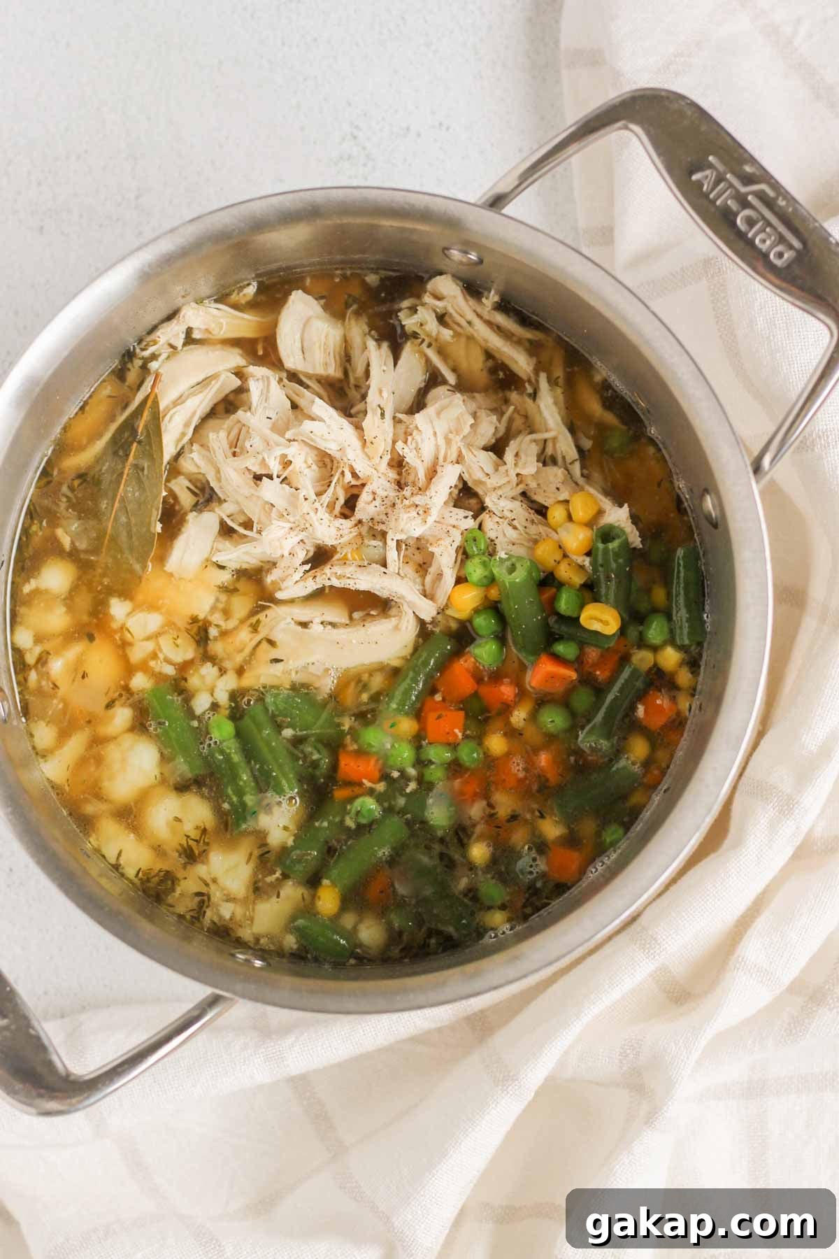 Dairy-Free, Gluten-Free Chicken Pot Pie Soup Recipe 7 Broth with shredded chicken, cooked cauliflower and frozen mixed vegetables in a stock pot.