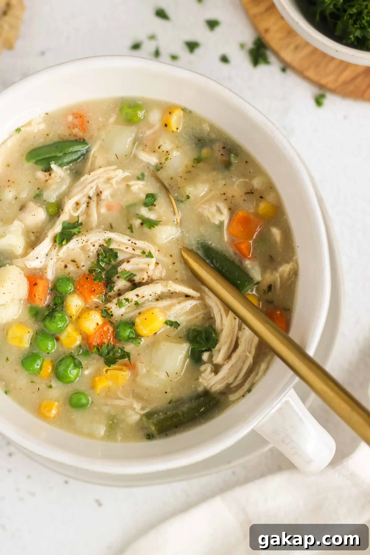 Dairy-Free, Gluten-Free Chicken Pot Pie Soup Recipe 10 Creamy chicken pot pie soup topped with fresh parsley and cracked pepper in a bowl with a gold spoon.