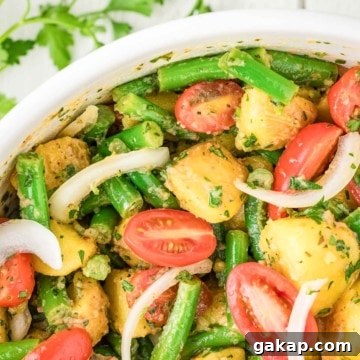 A bowl of potato salad with green beans, cherry tomatoes, sliced onions, and chopped herbs.