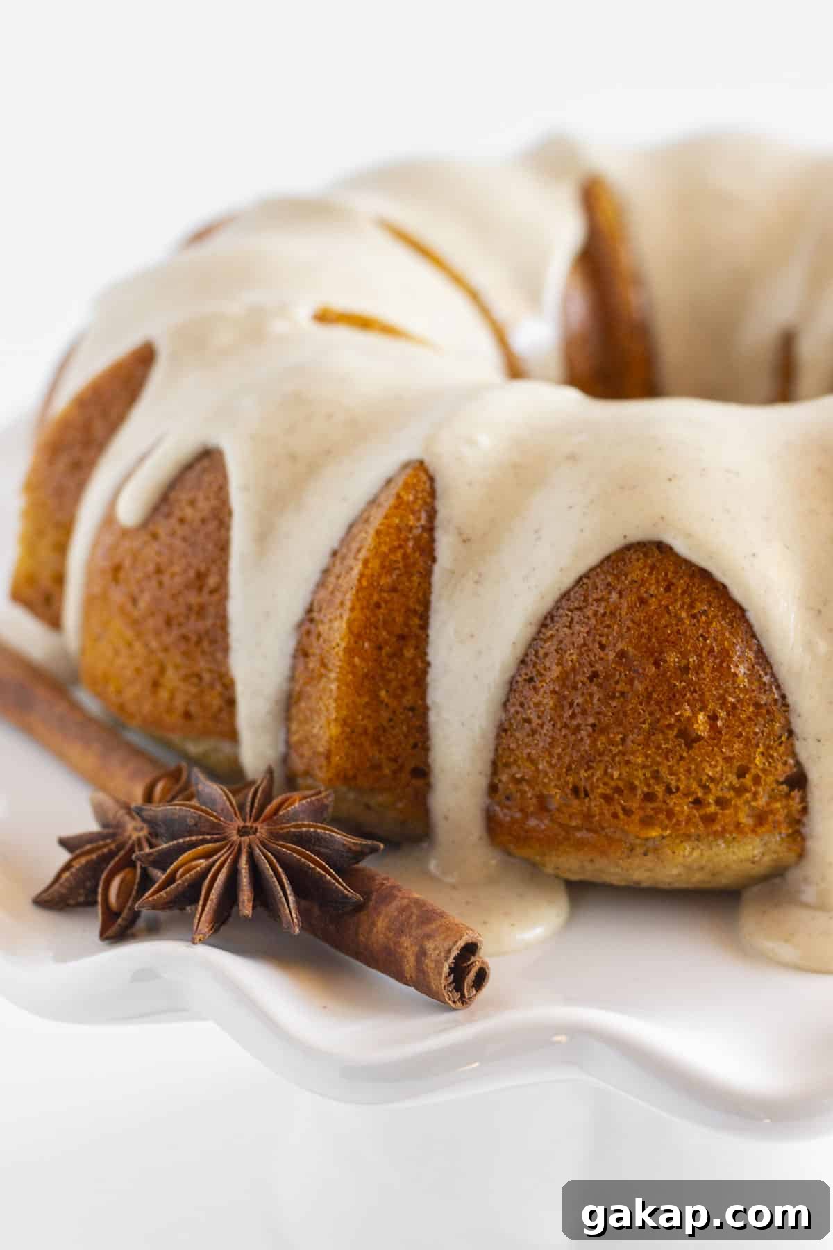 Moist Bundt Spice Cake Made with Cake Mix – Simple Holiday Dessert 2 A frosted spice bundt cake on a white plate.