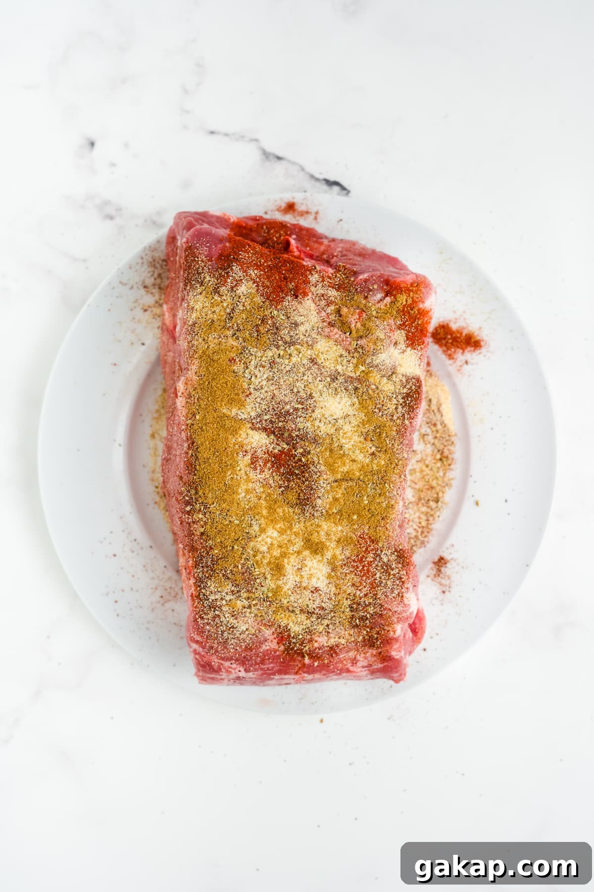 The pork on a plate with seasoning rubbed all over.