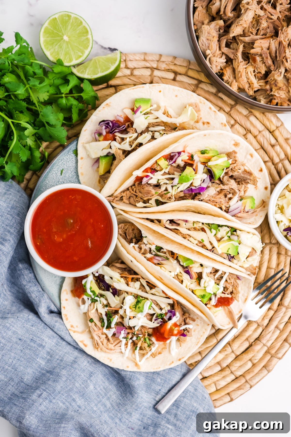 Slow cooker pork tacos on a plate with a ramekin of red salsa. 