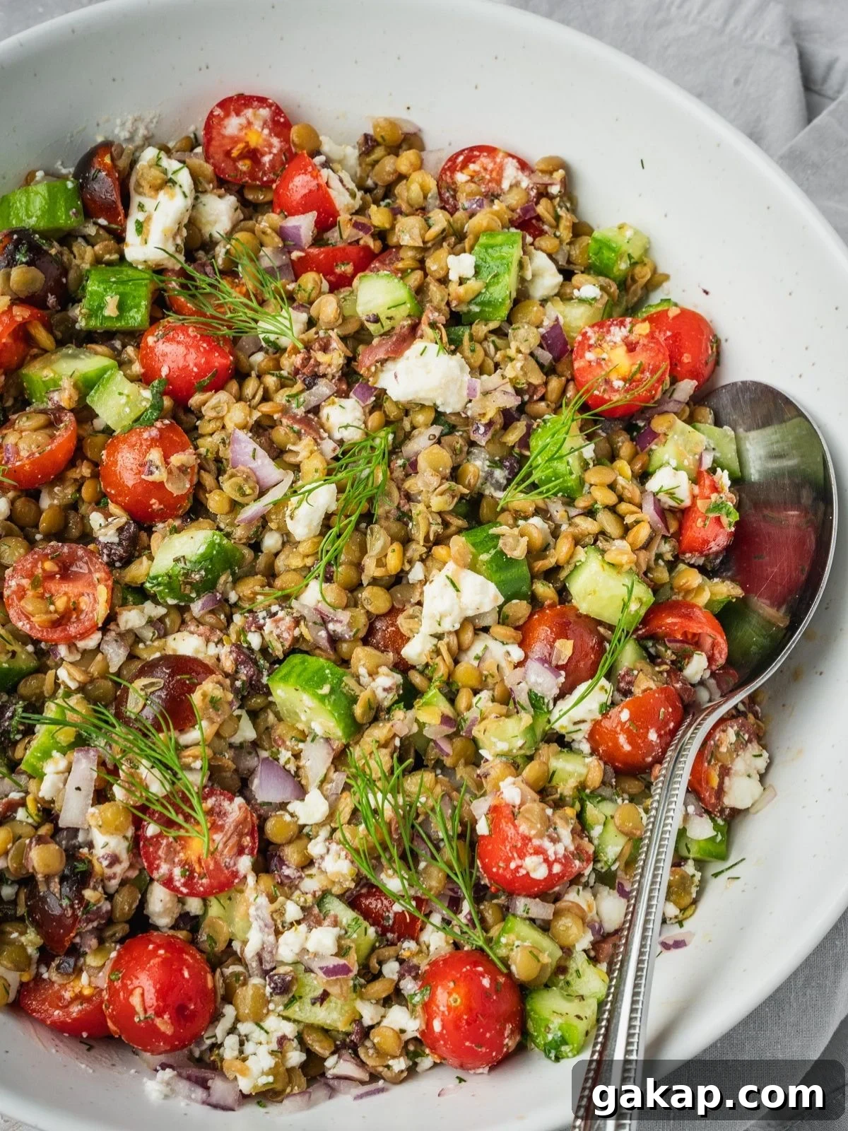 Greek lentil salad in a large bowl with sliced cherry tomatoes, cucumbers, feta, olives and herbs.