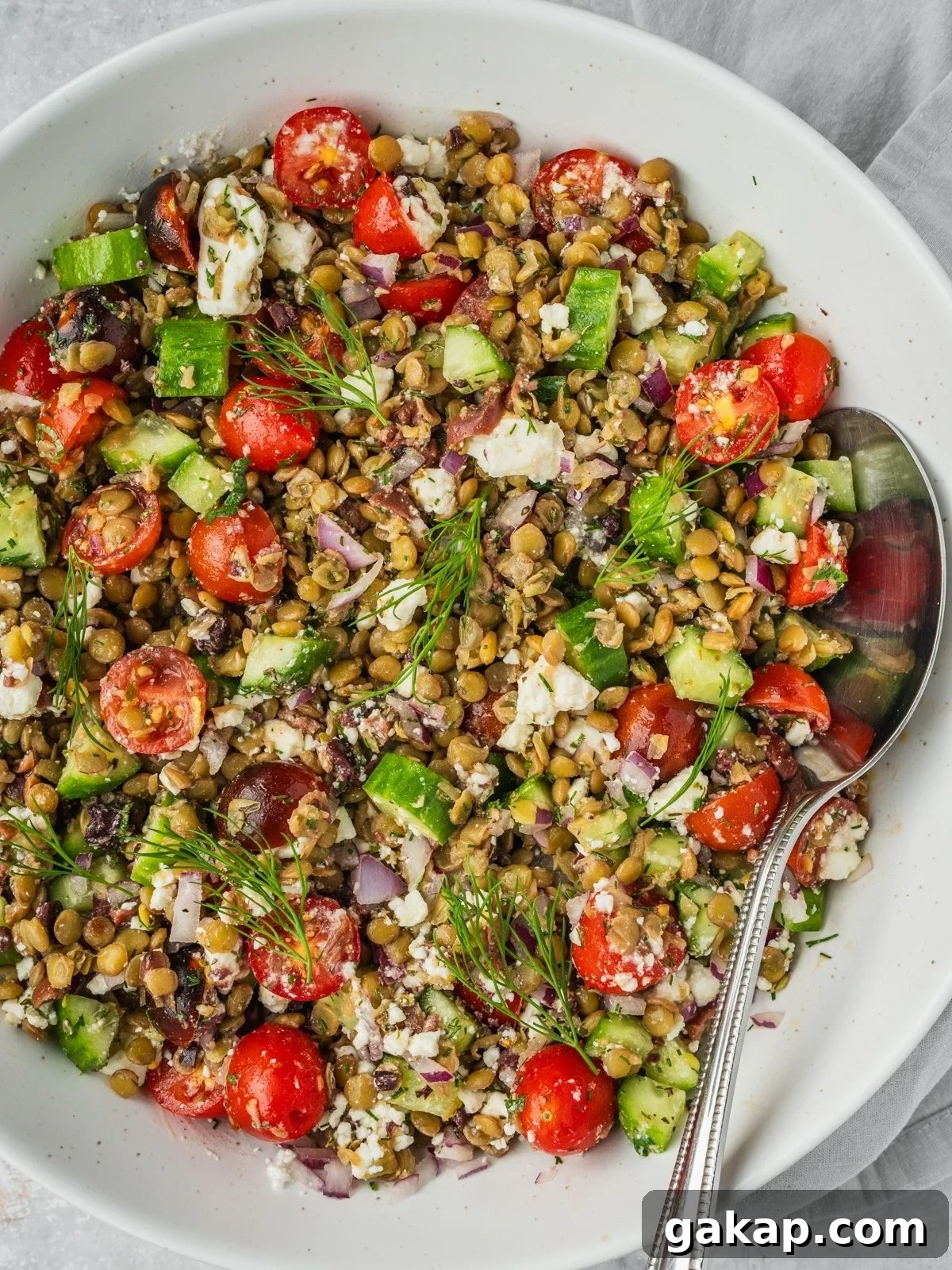 Greek lentil salad in a large bowl with sliced cherry tomatoes, cucumbers, feta, olives and herbs.
