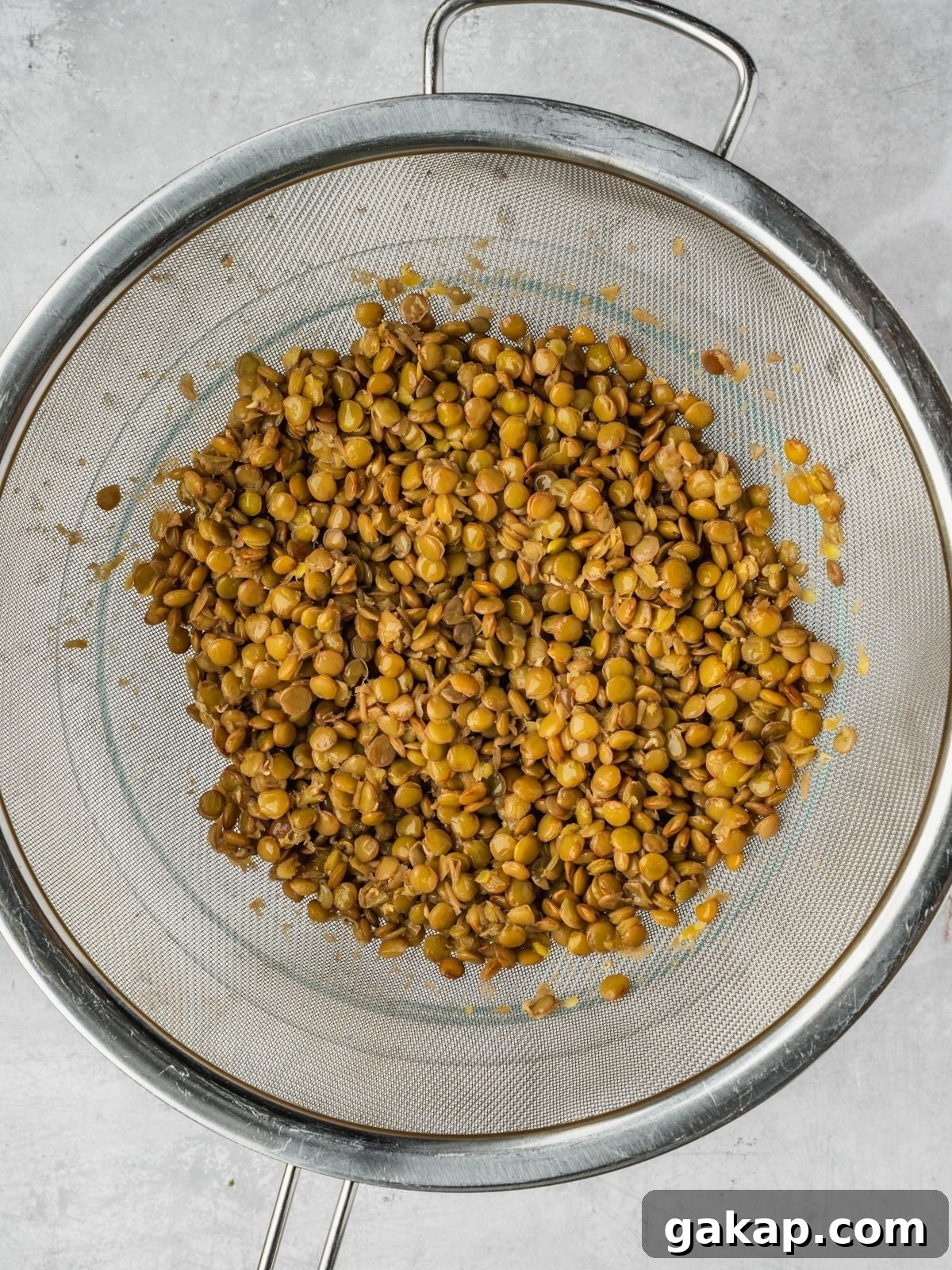Cooked lentils draining in a metal fine mesh sieve.