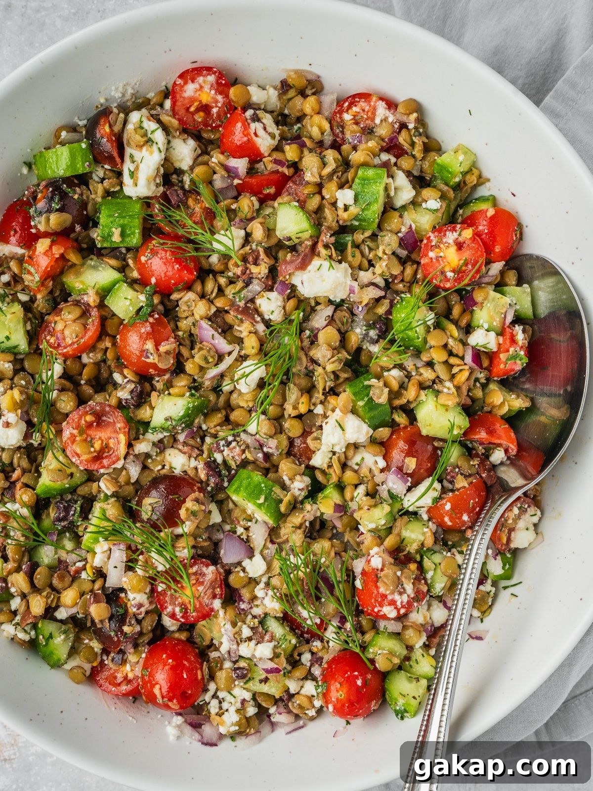 Greek lentil salad in a large bowl with sliced cherry tomatoes, cucumbers, feta, olives and herbs.