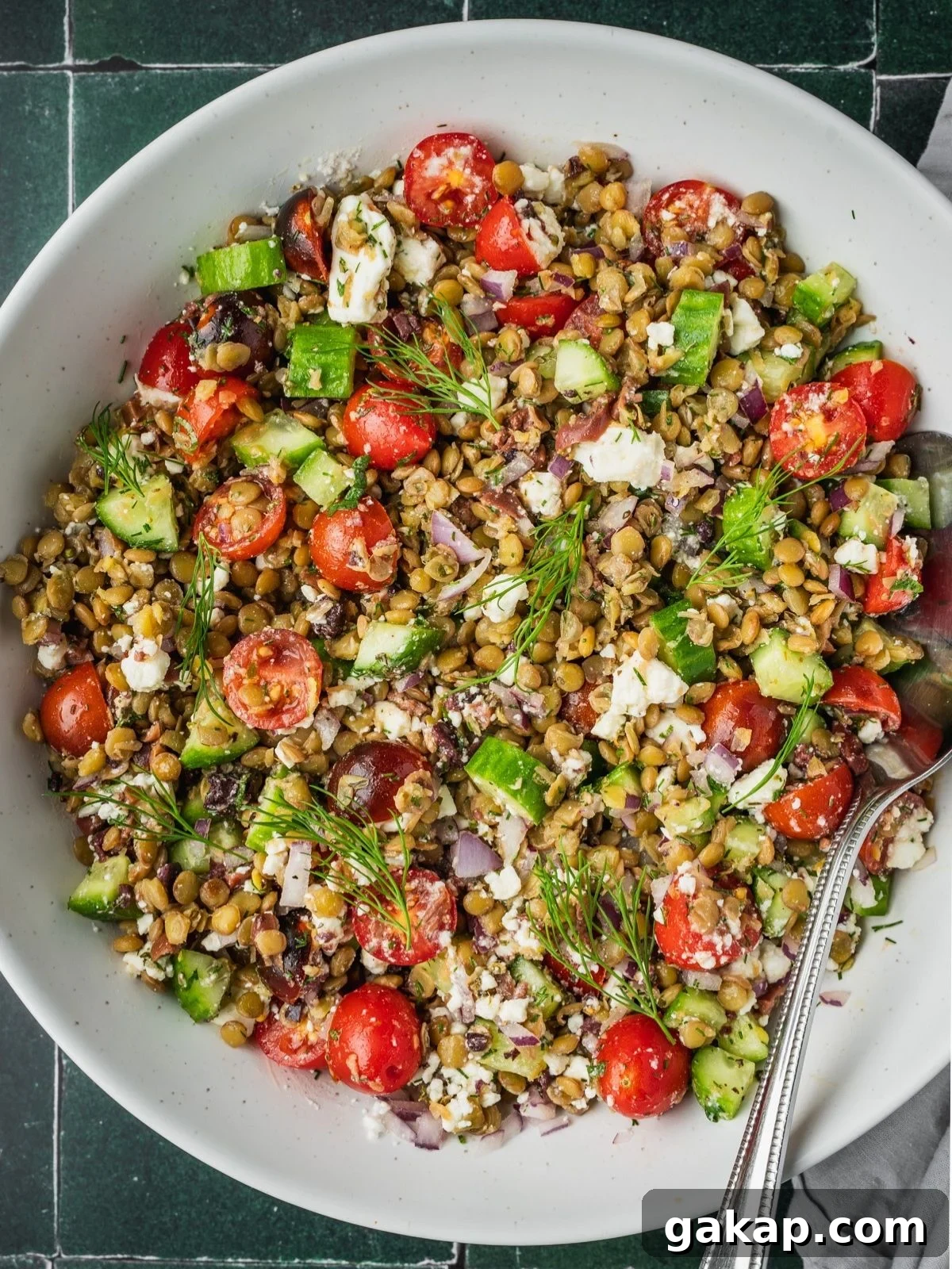 Greek-inspired lentil salad in a large bowl with sliced cherry tomatoes, cucumbers, feta, olives and herbs.