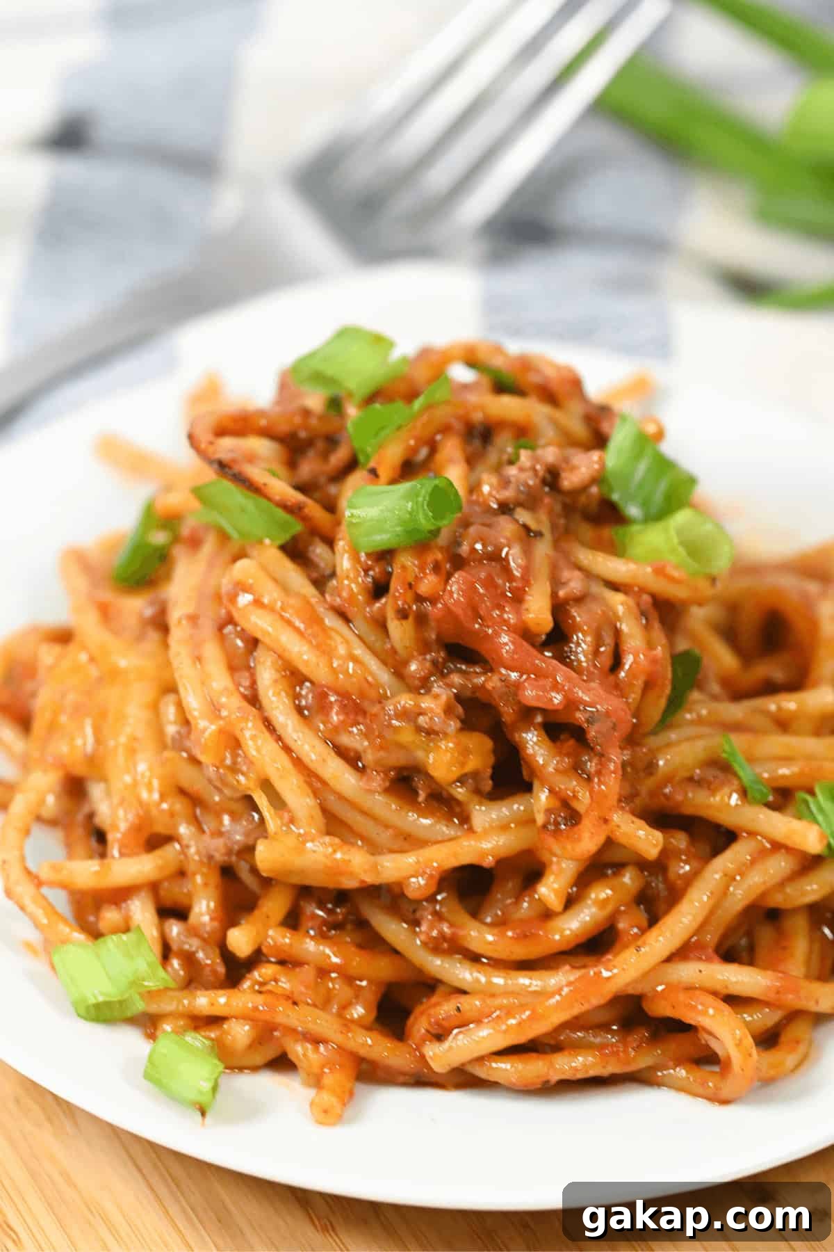 A plate of Mexican spaghetti topped with seasoned ground meat and garnished with chopped green onions.