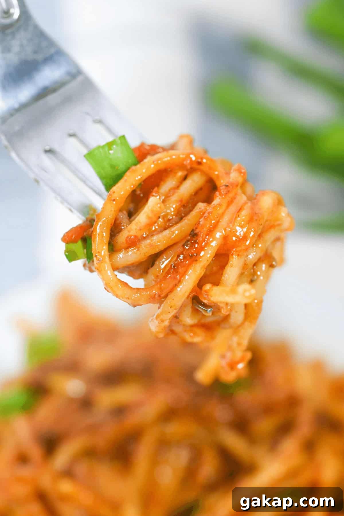 A fork holds a serving of the meal with adorned with zesty tomato sauce and vibrant green onions.