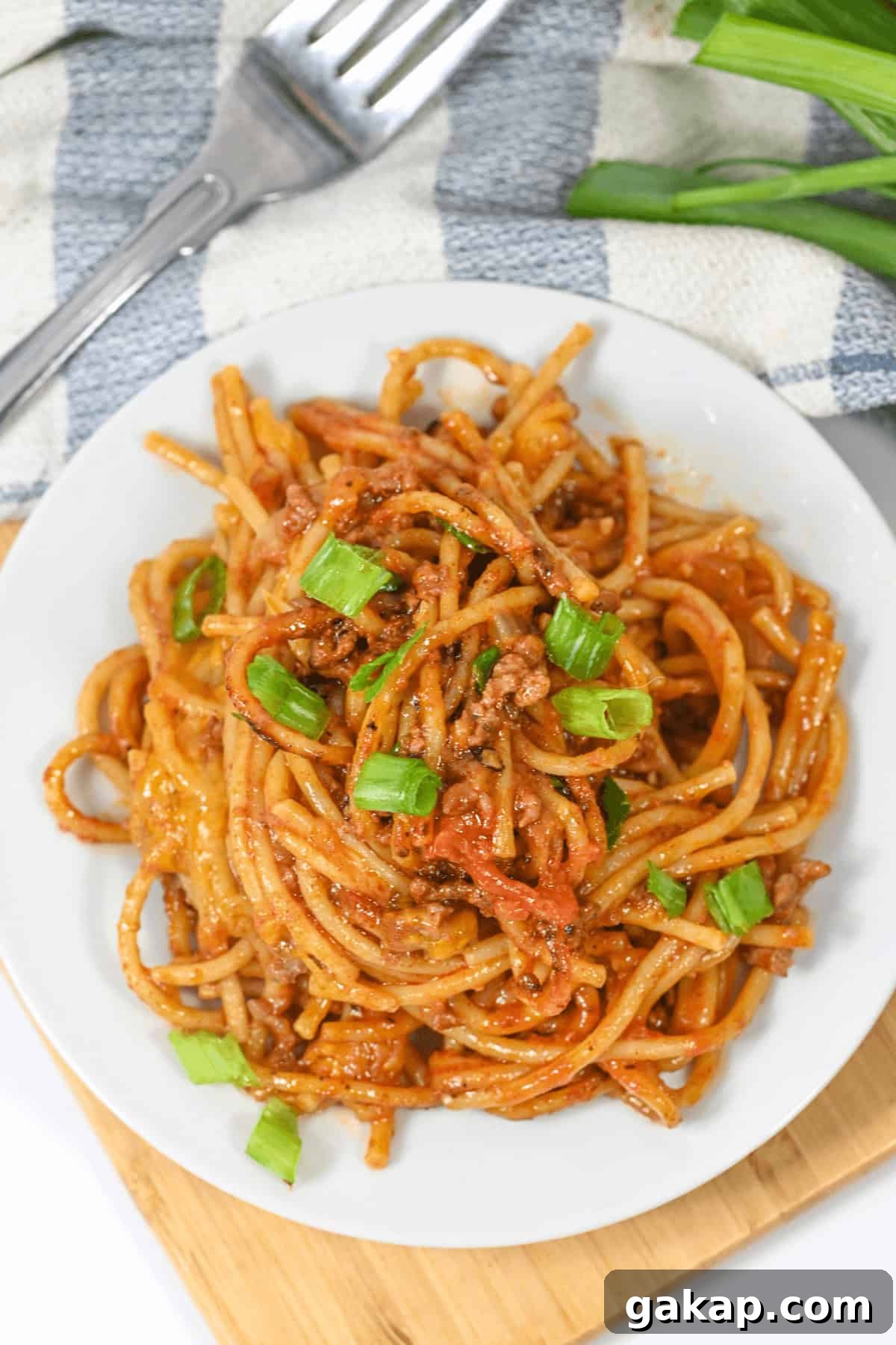 A plate of Mexican spaghetti with meat sauce, infused with vibrant flavors and topped with chopped green onions, sits invitingly next to a fork and fresh green onions.