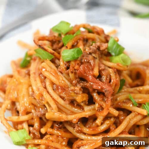 A plate of Mexican spaghetti topped with seasoned ground meat and garnished with chopped green onions.