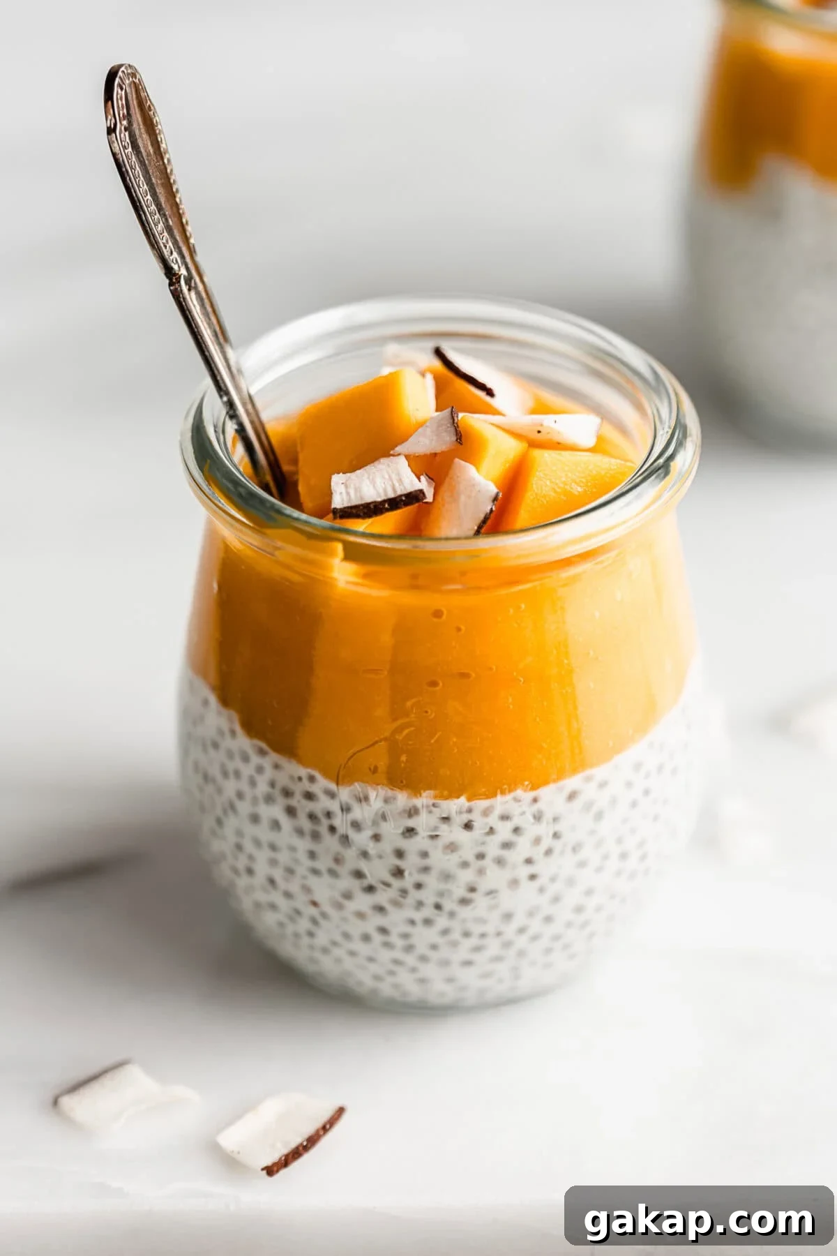 A cup of coconut chia pudding topped with mango puree, chunks of mango and coconut flakes.