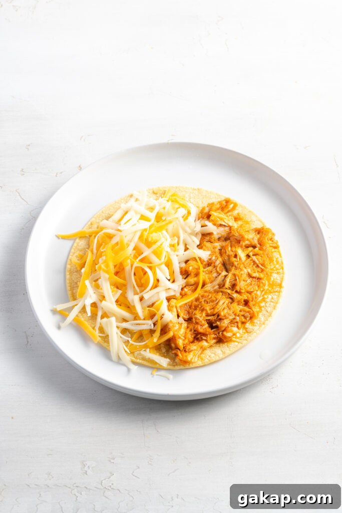 corn tortilla topped with chicken tinga and shredded cheese on a white plate before frying until crispy.