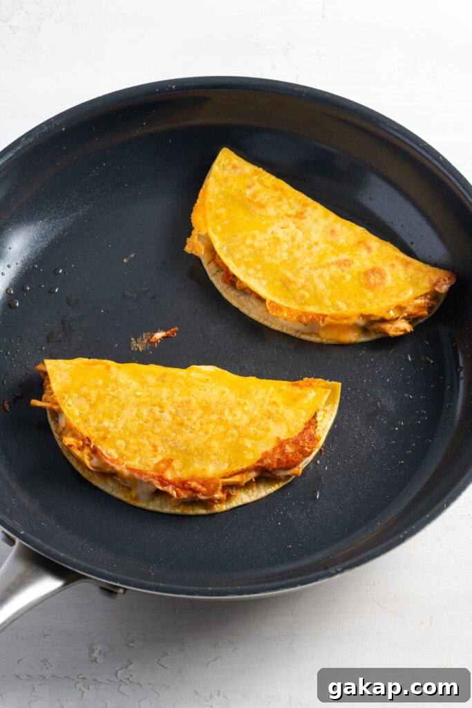 two crispy chicken tacos cooking in a skillet to get crispy.