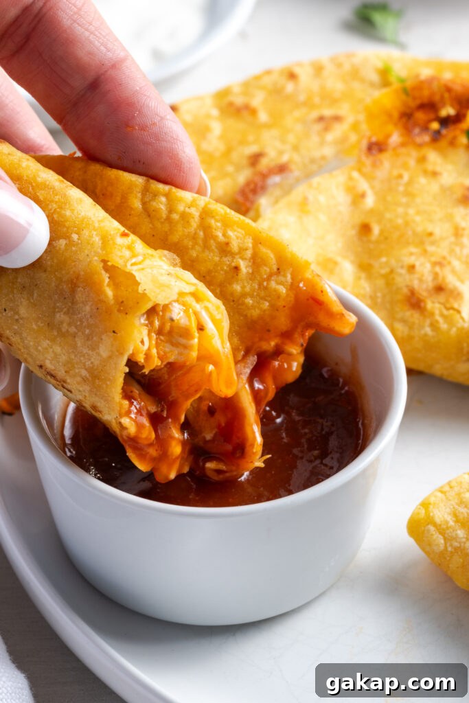 hand dipping a crispy chicken taco into a red sauce.
