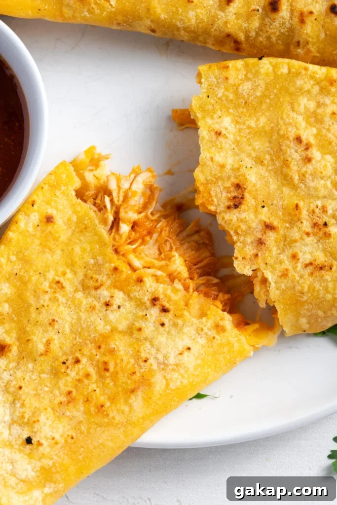 closeup shot of a crispy chicken and cheese taco that has been pulled into two halves with the chicken and cheese filling pulled between the sides.