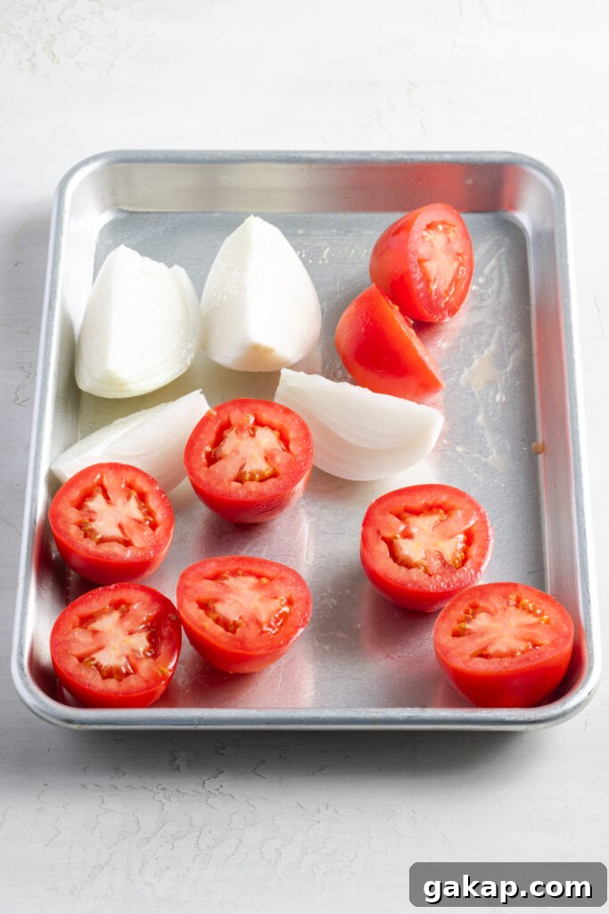 halved tomatoes and a quartered white onion on a silver rimmed baking sheet.