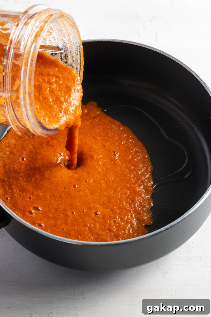 action shot of the spicy tomato tinga sauce being poured from the blender into a skillet with oil.