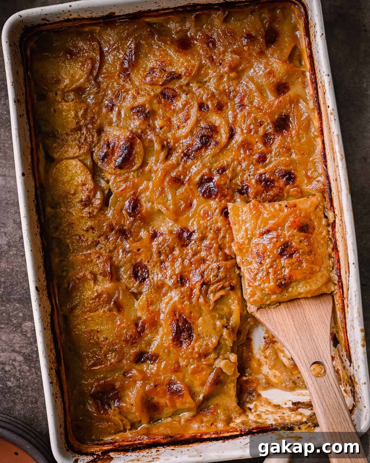 cheesy vegan scalloped potatoes in casserole pan with slice being lifted up by a spatula