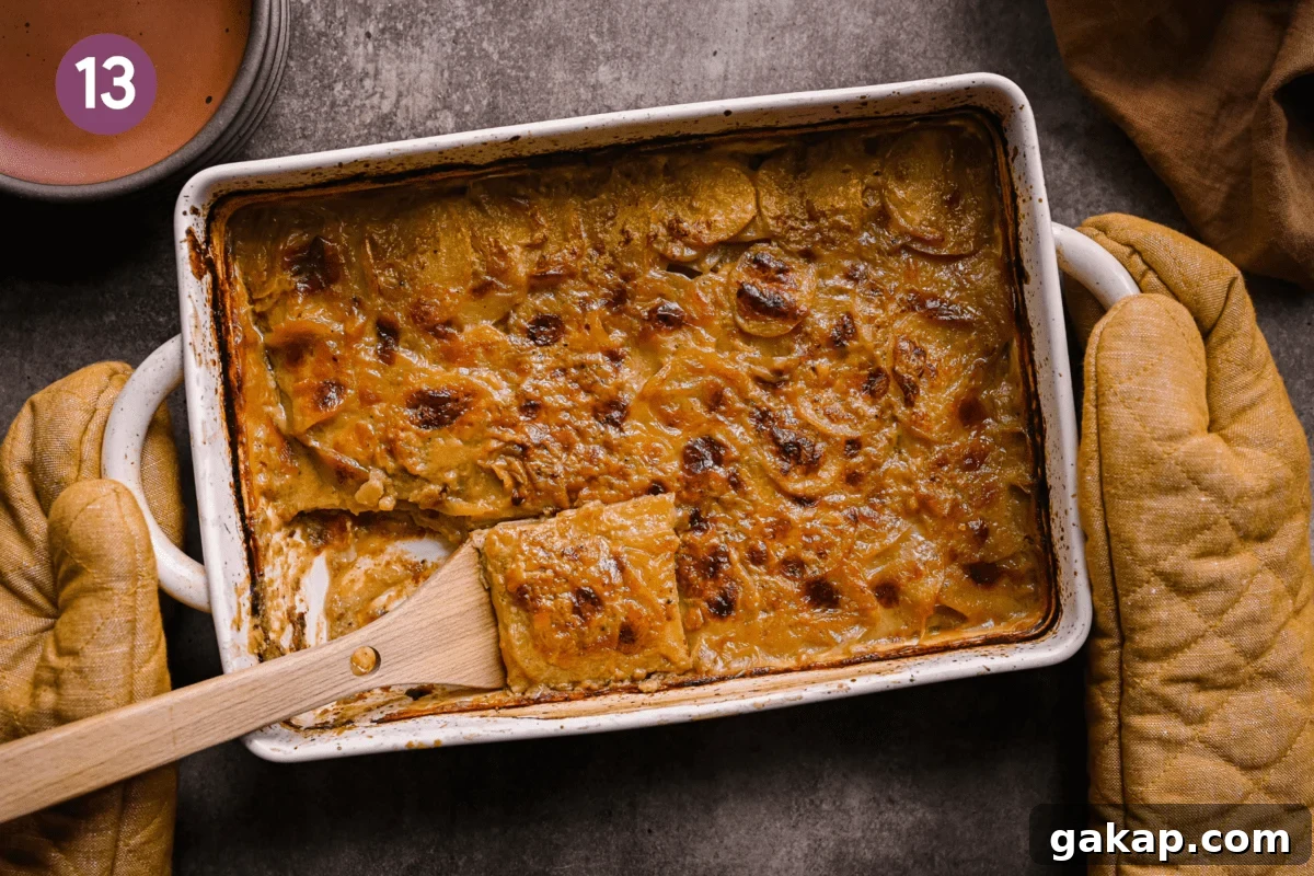 hands with yellow oven mitts placing a pan of vegan scalloped potatoes down on a brown table.
