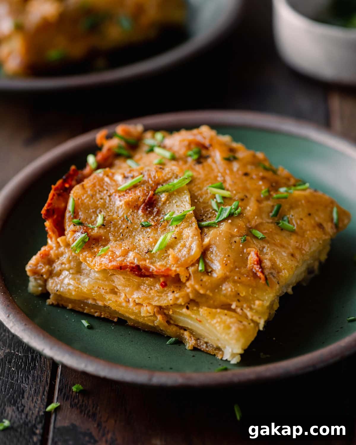 slice of vegan scalloped potatoes topped with chives on green plate
