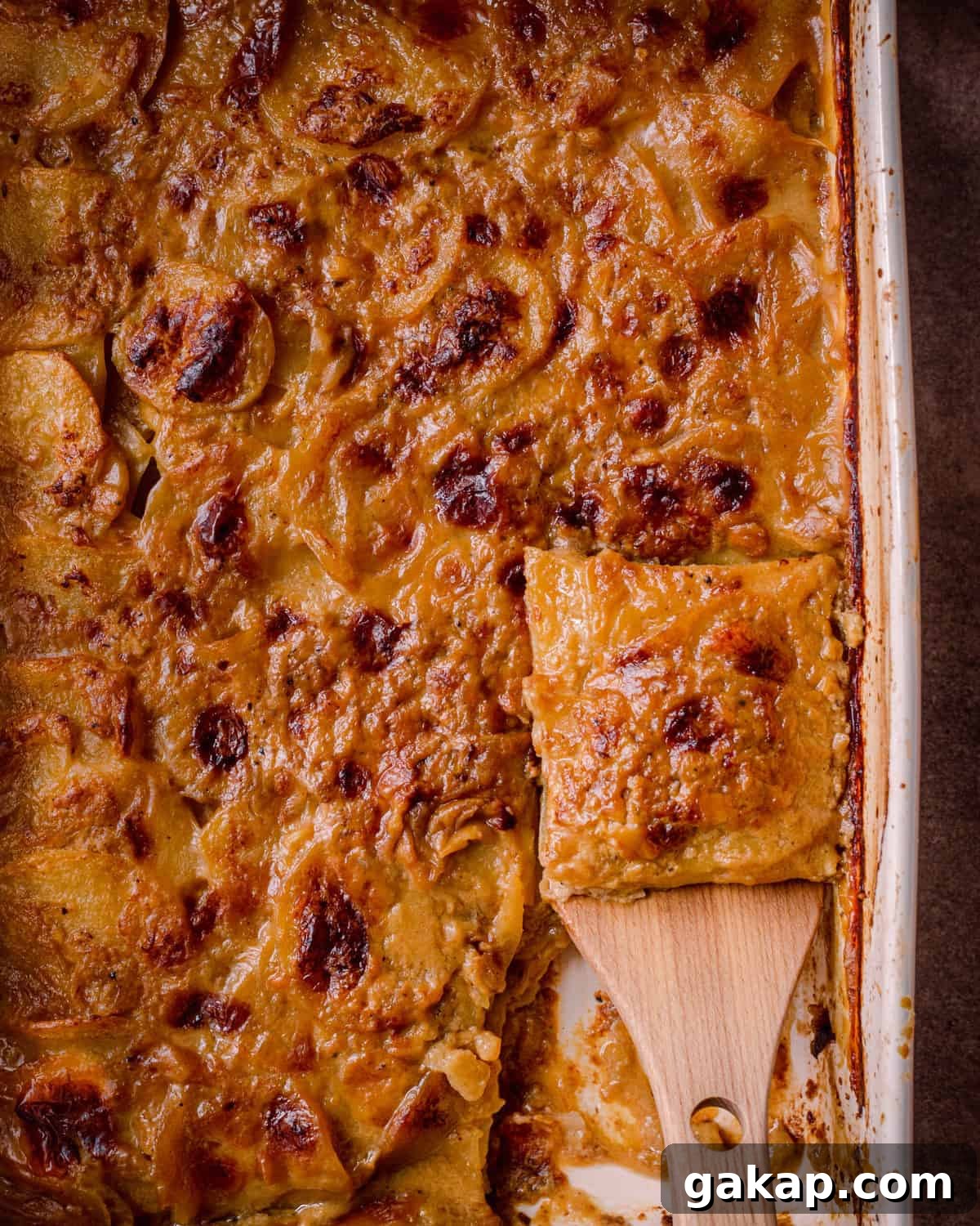 cheesy vegan scalloped potatoes in casserole pan with slice being lifted up by a spatula