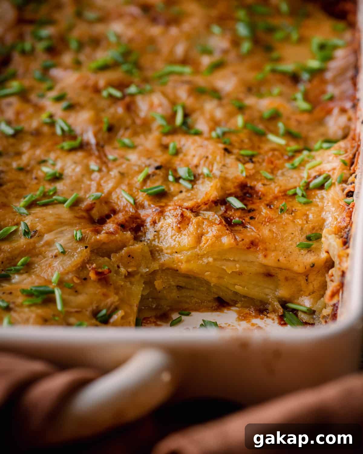 closeup shot of cheesy vegan scalloped potatoes in casserole pan topped with chives