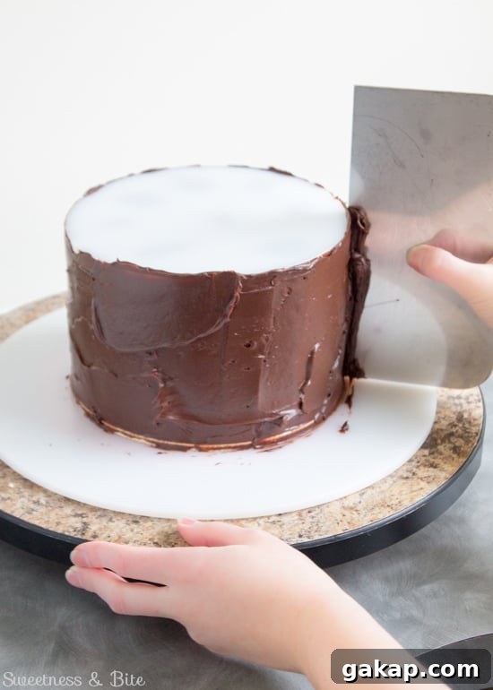 Perfect Ganache for Cakes: Step-by-Step Guide and Tips 7 A metal scraper being used to scrape off the excess ganache as the turntable is turned.